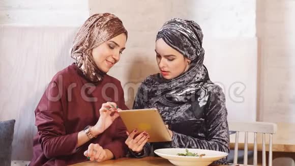 两个漂亮的穆斯林女人在咖啡厅里用桌子视频的预览图