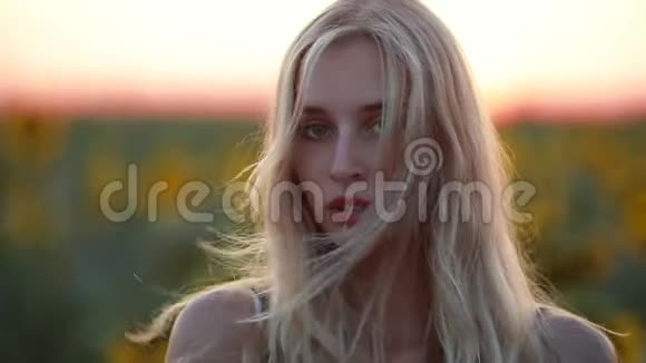 女人在田野里看着夕阳看着镜头风吹着她的头发视频的预览图
