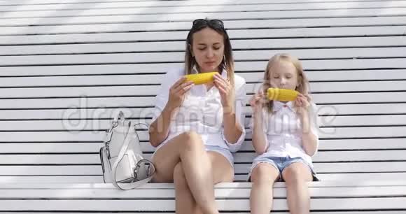 年轻的母亲和她的女儿夏天在公园里吃煮玉米视频的预览图
