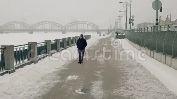 一个人在冬天的河边散步拍摄于一架无人机在它前面移动视频的预览图