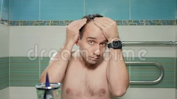 年轻有魅力的男人在酒店房间的浴室里检查一条后退的发际线他擦奶油来治疗脱发视频的预览图