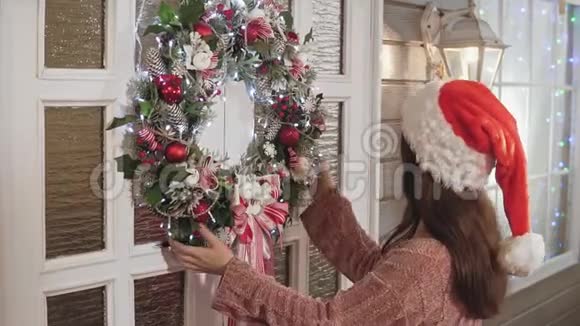 戴着帽子戴着圣诞花环门上戴着球的漂亮女人视频的预览图