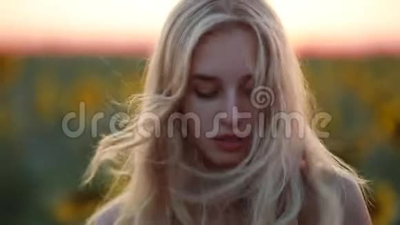 女人在田野里看着夕阳看着镜头风吹着她的头发视频的预览图