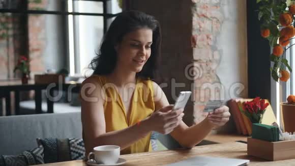 持银行卡的咖啡厅用智能手机在线付款的年轻女子视频的预览图