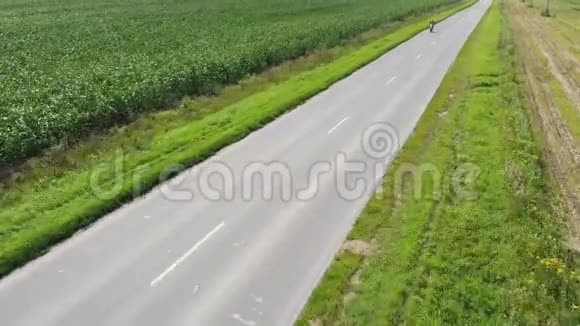 绿色玉米地的鸟瞰图骑摩托车的小孩在玉米地上的柏油路上骑摩托车视频的预览图