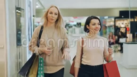 漂亮的金发女郎正在和她漂亮的女朋友逛街聊天微笑着在商场里散步然后看着视频的预览图