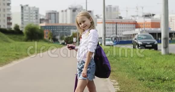 一个可爱的金发女孩站在城市道路上的街道上带着一辆滑板车视频的预览图