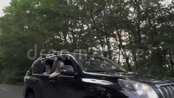 黑色的汽车慢慢地骑着马路三个人的公司正在旅行女孩把头伸出车窗外视频的预览图