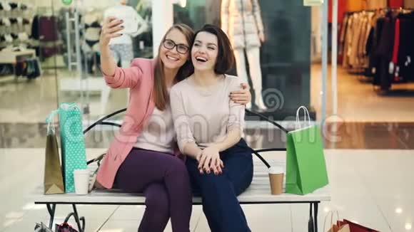 漂亮的年轻女性正在自拍使用智能手机相机坐在购物中心的长凳上玩得很开心现代视频的预览图
