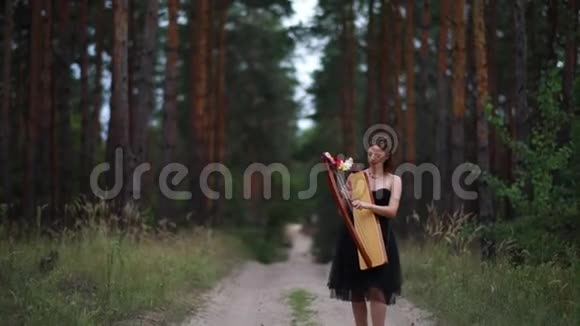 女竖琴手走在森林里在松树的背景下弹奏竖琴视频的预览图