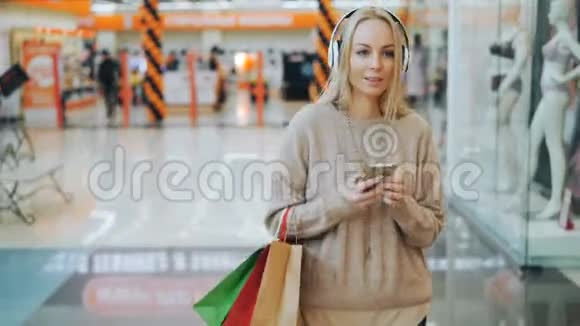 一位金发碧眼的年轻快乐女士正在听音乐一边听耳机一边使用智能手机视频的预览图