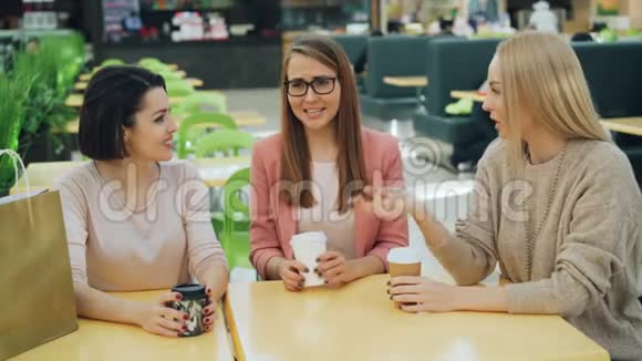 一群快乐的年轻女士在购物中心的咖啡馆里坐在桌子旁一边喝着饮料一边笑视频的预览图