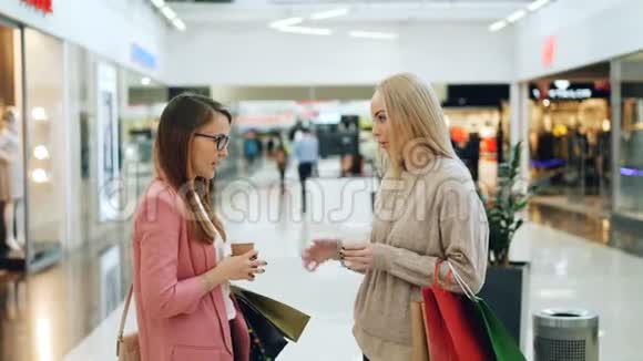 快乐的女学生在购物中心站在一起拿着袋子和外卖饮料谈笑风生视频的预览图