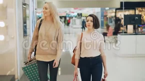 漂亮的年轻女士朋友们在宽敞的大商店里散步一边聊天一边微笑着享受购物日视频的预览图