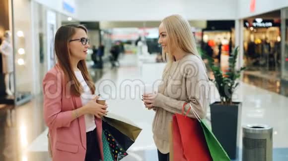 漂亮的女孩在购物中心聊天拿着纸袋和外卖咖啡微笑青年生活方式视频的预览图