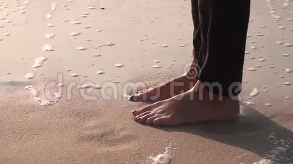 女孩穿着黑色牛仔裤的腿在潮湿的沙滩上洗着冲浪用泡沫挥手视频的预览图