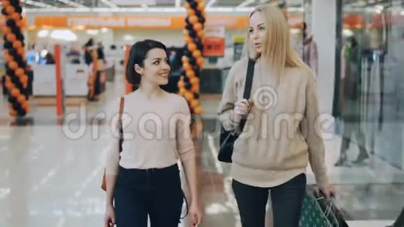 多莉拍摄了美丽的女孩学生聊天在购物中心步行与纸袋在空闲时间消费主义视频的预览图