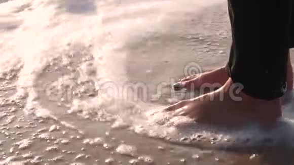 女孩穿着黑色牛仔裤的腿在潮湿的沙滩上洗着冲浪用泡沫挥手视频的预览图