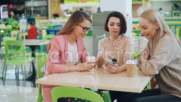 快乐的女士们一起坐在咖啡馆里看着智能手机屏幕然后一起聊天然后做着击掌和大笑视频的预览图