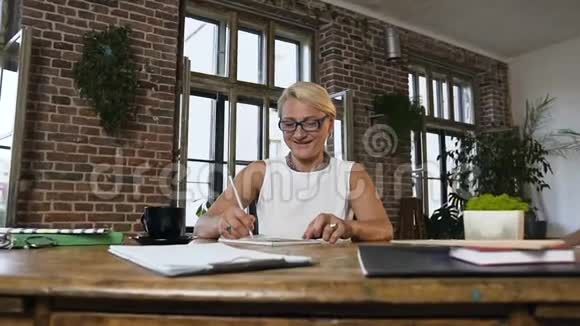 漂亮的中年妇女戴着眼镜坐在木桌上拿着纸文件工作而她可爱的孙子孙女视频的预览图