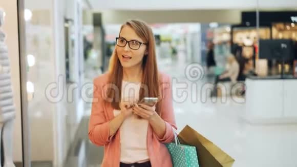 漂亮的年轻女士在购物中心使用智能手机触摸屏幕然后环顾四周看看新的系列视频的预览图