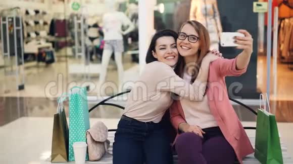 漂亮的年轻女士正在一起自拍使用智能手机坐在购物中心休息和玩得开心视频的预览图