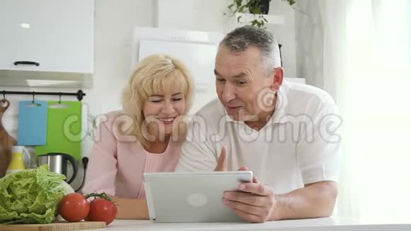 退休家庭在公寓厨房平板电脑上观看视频视频的预览图