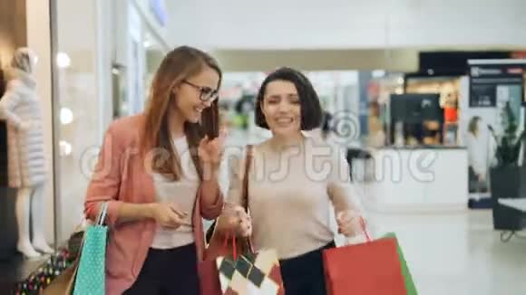 漂亮的年轻女人拿着包在购物中心走来走去谈笑风生视频的预览图