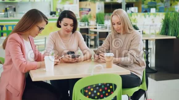 漂亮的年轻女性正在使用智能手机坐在咖啡馆的桌子上看屏幕现代技术青年视频的预览图