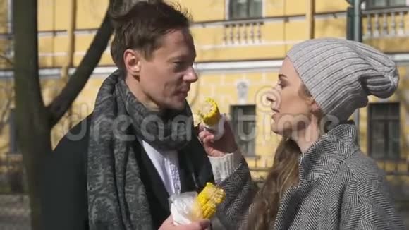 可爱的夫妇在外面吃黄玉米在阳光明媚的春天在城里接吻视频的预览图