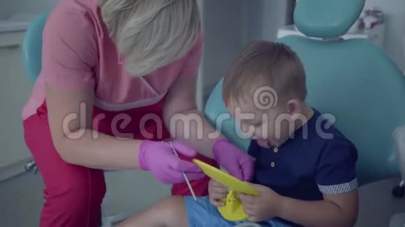 戴着医用口罩和手套的牙医准备检查椅子上坐着镜子的无忧无虑的小男孩的牙齿视频的预览图