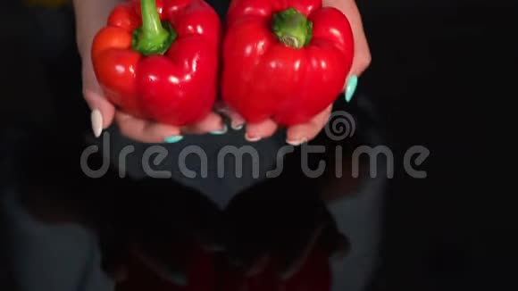 女人的特写黑色背景上拿着成熟的红椒慢动作视频的预览图