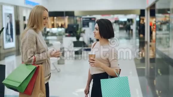 有魅力的年轻女性在购物中心谈论着去买咖啡和纸袋趋势视频的预览图