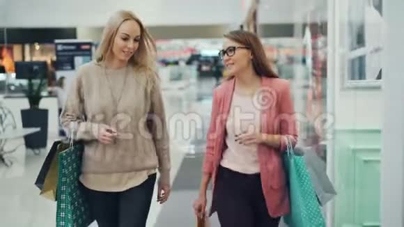 快乐的女人在商店购物中心里拎着纸袋一边说话一边打手势女孩们穿着视频的预览图