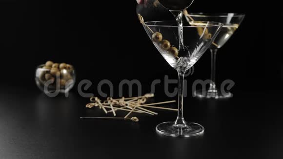豪华马提尼手把甜马提尼倒入用橄榄和鸡尾酒棒装饰的桌子上的空杯子里视频的预览图