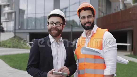 幸福的建筑工人和商人站在现代建筑背景下看镜头的肖像视频的预览图