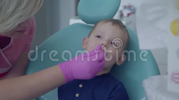 牙医准备检查坐在牙科办公室椅子上的无忧无虑的小男孩的牙齿女性专业人员视频的预览图