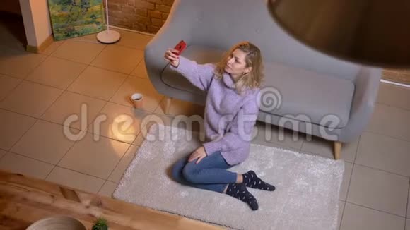 一位成年白种人金发女性坐在室内沙发上打电话自拍视频的预览图