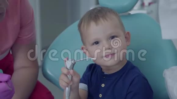 牙医准备检查坐在牙科办公室椅子上的无忧无虑的小男孩的牙齿女性专业人员视频的预览图