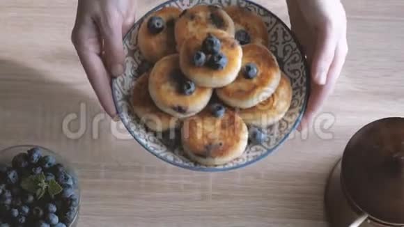女性用手把一片薄荷叶放在sirniki传统的俄式薄饼上上面有白干酪和蓝莓视频的预览图