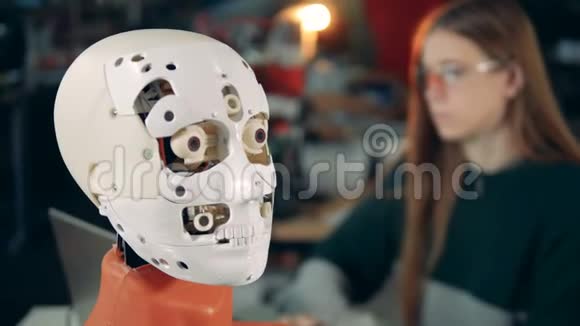 特写一个机器人的面部表情和一位女士在后台工作视频的预览图