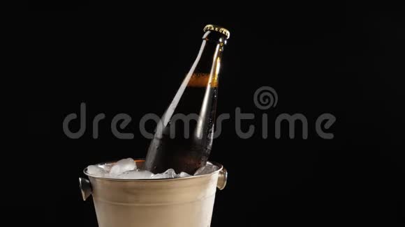 新鲜啤酒手拿一个棕色的瓶子和美味的工艺啤酒从一个桶里拿出来在黑色的背景下放着冰冷的真正的冰视频的预览图