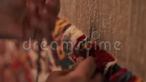 一位老年妇女缝制东方地毯在织布机后面的特写镜头视频的预览图