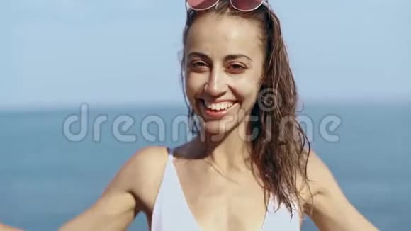 外面的美丽年轻性感女人的肖像穿着白色比基尼站在海边的海湾上靠在蓝色的大海上视频的预览图