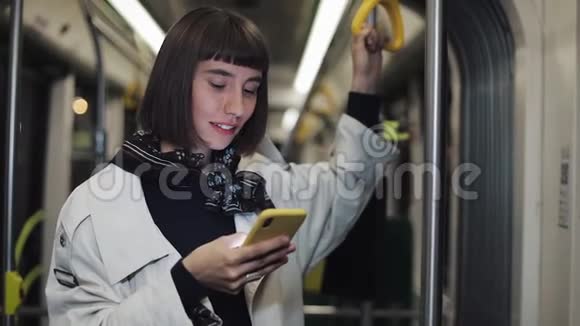 年轻时髦女性的肖像握着扶手使用智能手机站在公共交通工具上城市灯光视频的预览图