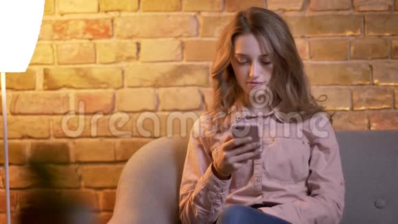 年轻迷人的少女在舒适的家中用智能手机工作开心地笑在镜头中的肖像视频的预览图