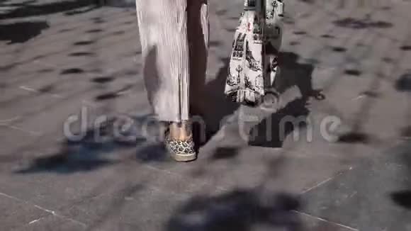 在阳光明媚的日子里穿着米色裤子和背心的纤细的女性腿穿过公园视频的预览图