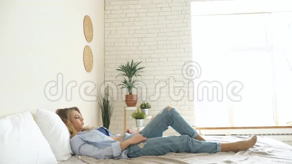 穿牛仔裤的女孩坐在床上双手伸展视频的预览图