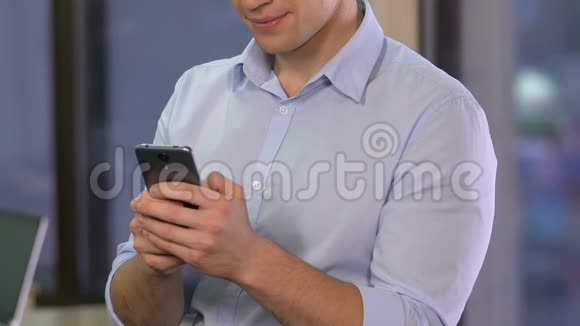 年轻的微笑男子在办公室里滚动智能手机在约会网站上聊天视频的预览图