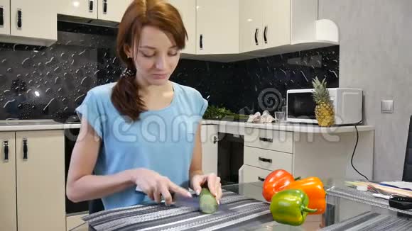 年轻女子在厨房里用刀切新鲜的绿色黄瓜健康的生活方式和饮食观念视频的预览图